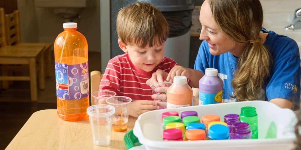 A preschool teacher helps a young child with an art project.