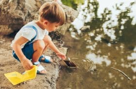 Preschool boy playing with a homemade boat in a local pond