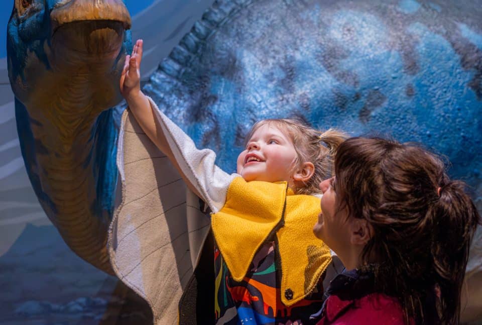 Toddler child petting play dinosaur at New Horizon Academy's dinosaur exhibit at the Minnesota Children's Museum