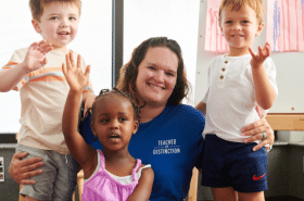 A teacher with three young children smile and wave
