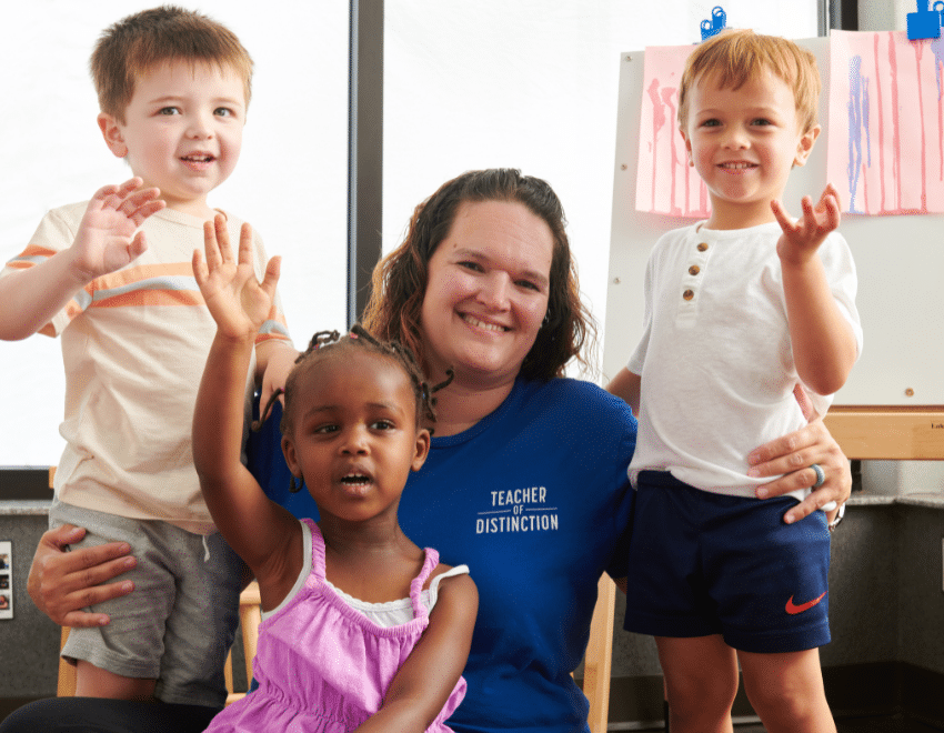 A teacher with three young children smile and wave